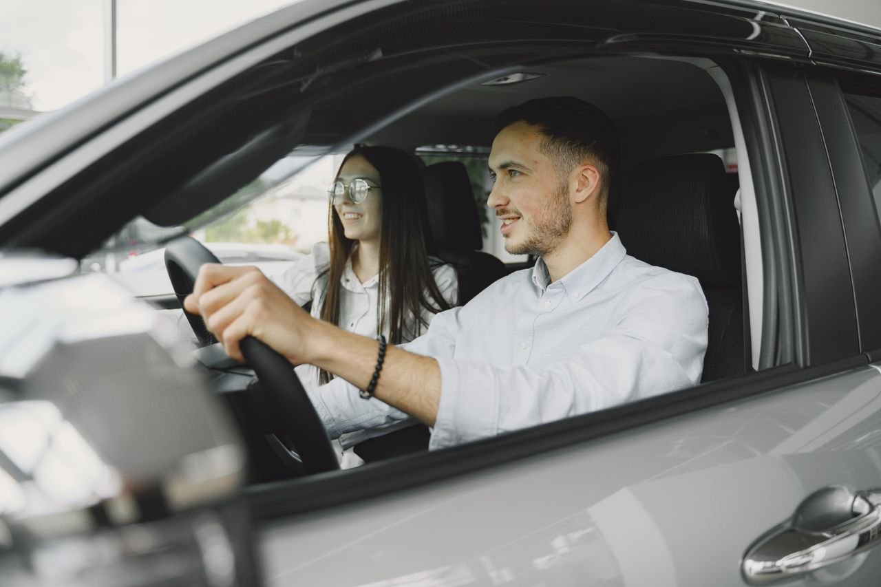 A young couple smiling while driving together in a modern car interior.